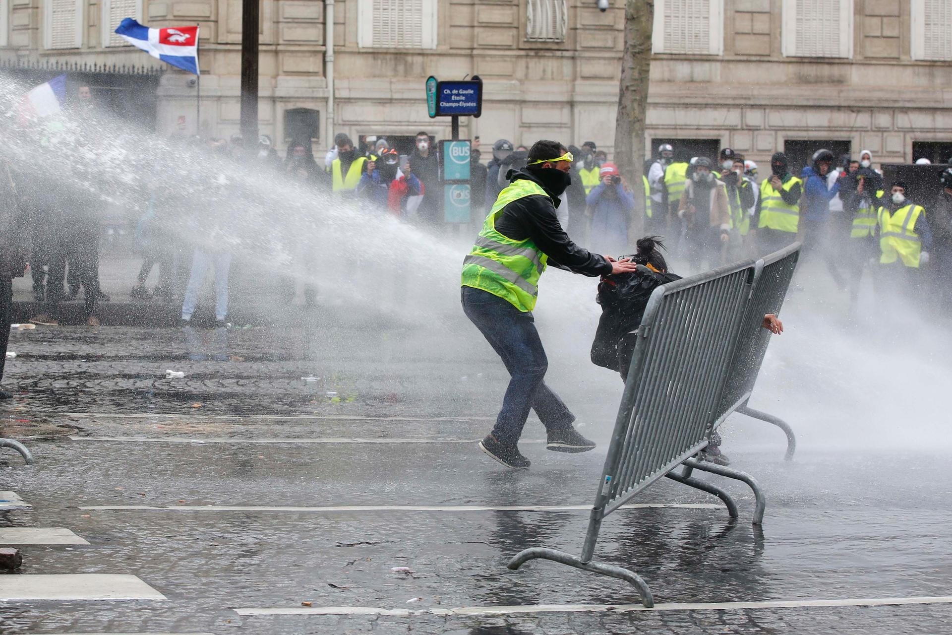 Ein Demonstrant eilt einer Demonstrantin zu Hilfe, während Polizisten Wasserkanonen einsetzen.