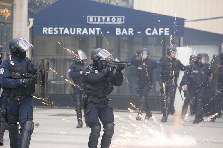 Ein Polizist zielt mit einer Flashball auf Demonstranten.