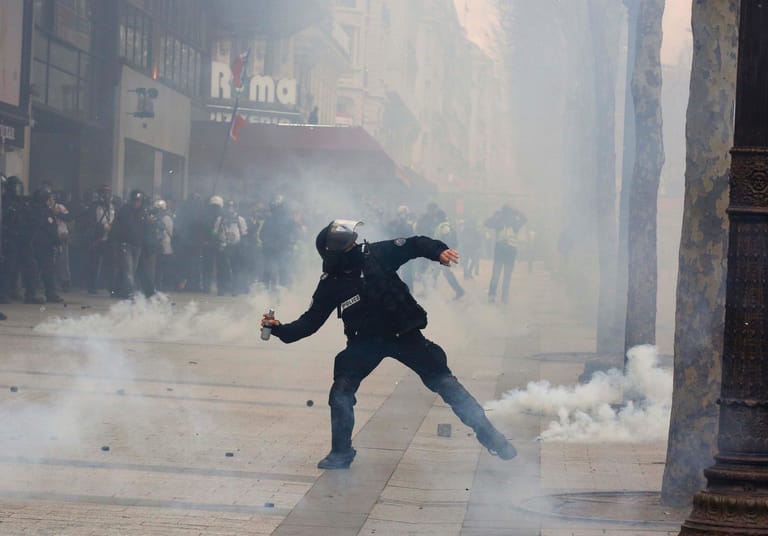 Ein Polizist wirft Tränengas auf Demonstranten auf dem Champs-Élysées.