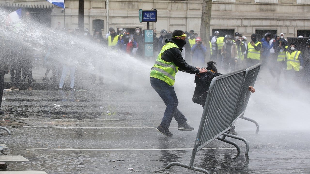 Ein Demonstrant eilt einer Demonstrantin zu Hilfe, während Polizisten Wasserkanonen einsetzen.