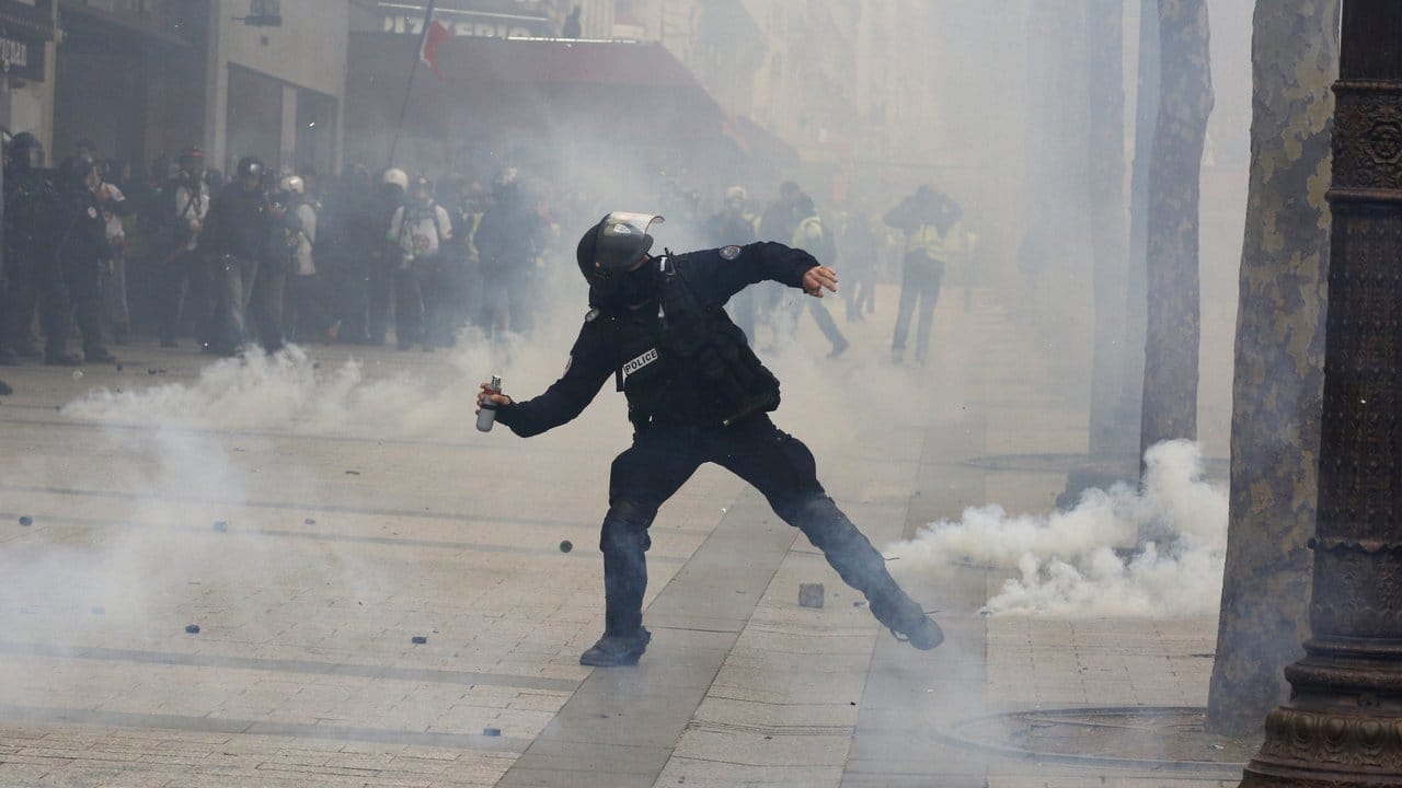 Ein Polizist wirft Tränengas in Richtung der demonstrierenden "Gelbwesten" auf den Champs-Elysees.