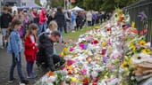 Trauernde Menschen legen am Botanischen Garten von Christchurch Blumen nieder.