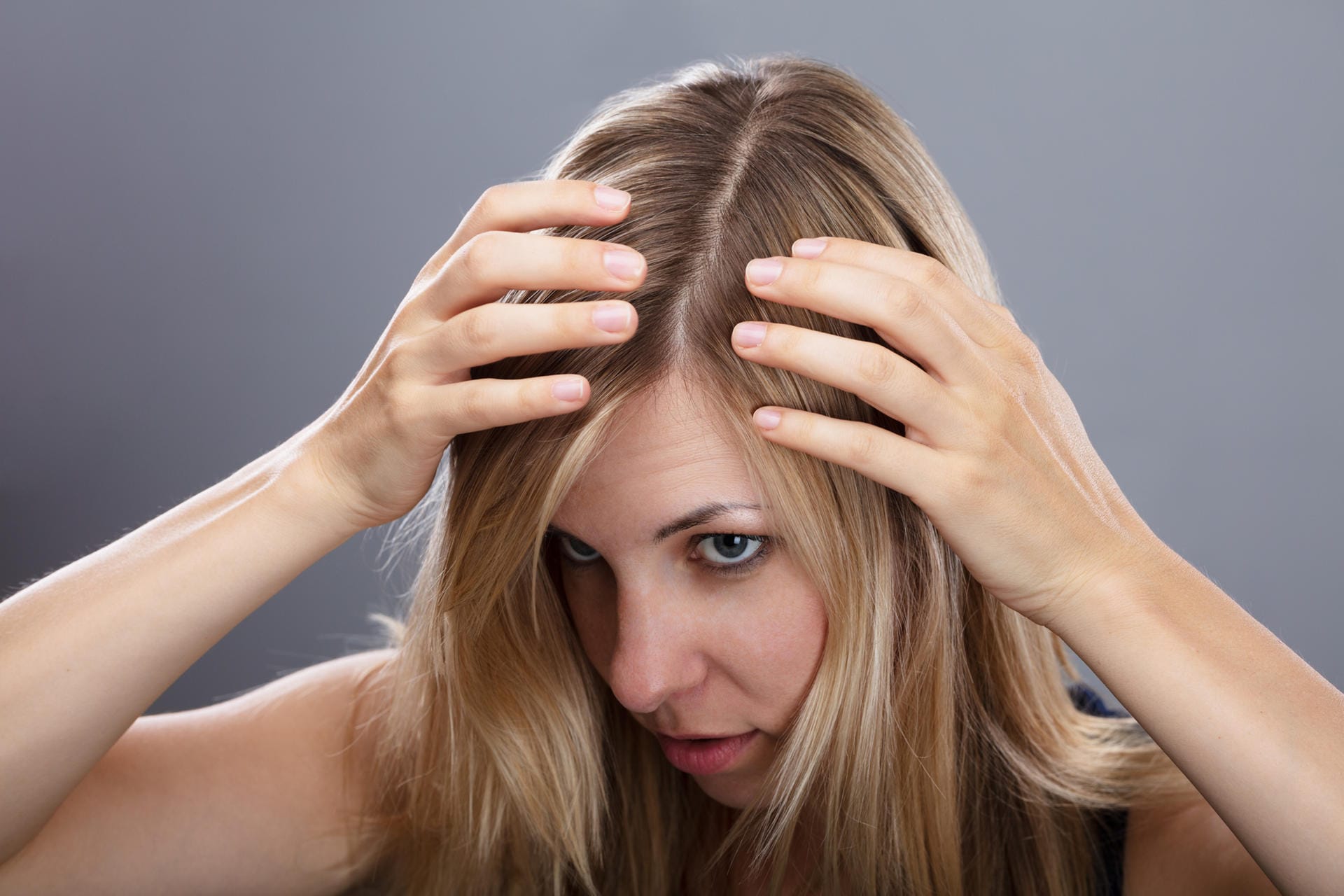 Frau betrachtet ihre Haare: Vor dem Färben zuhause, sollten Sie Ihre Haare ein bis zwei Tage nicht waschen.