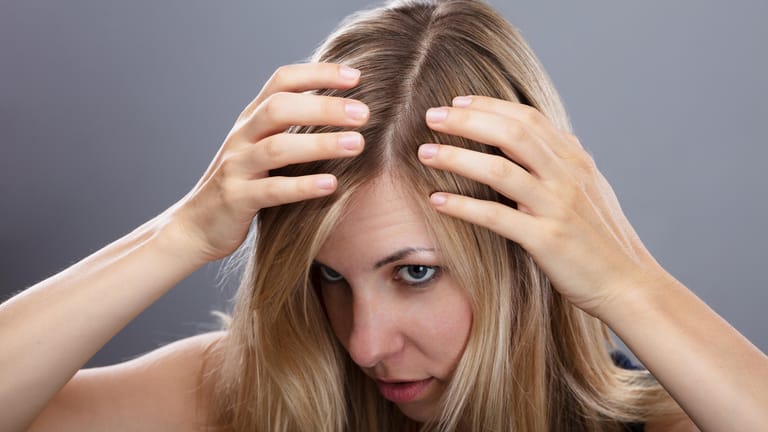 Frau betrachtet ihre Haare: Vor dem Färben zuhause, sollten Sie Ihre Haare ein bis zwei Tage nicht waschen.