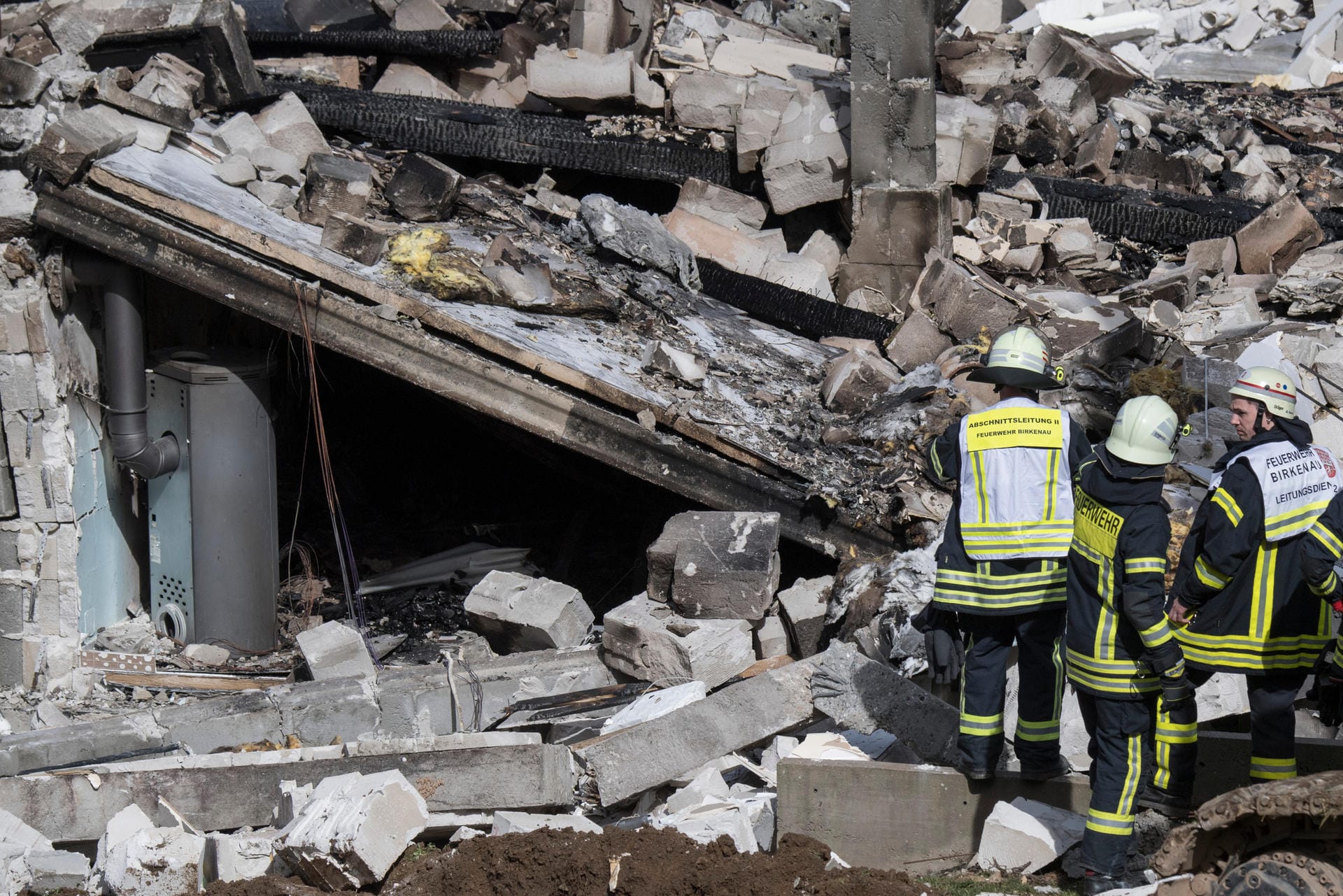 Rettungskräfte von Feuerwehr und technischem Hlfswerk (THW) stehen vor den Trümmern eines Wohnhauses in einem Ortsteil von Birkenau in Südhessen.