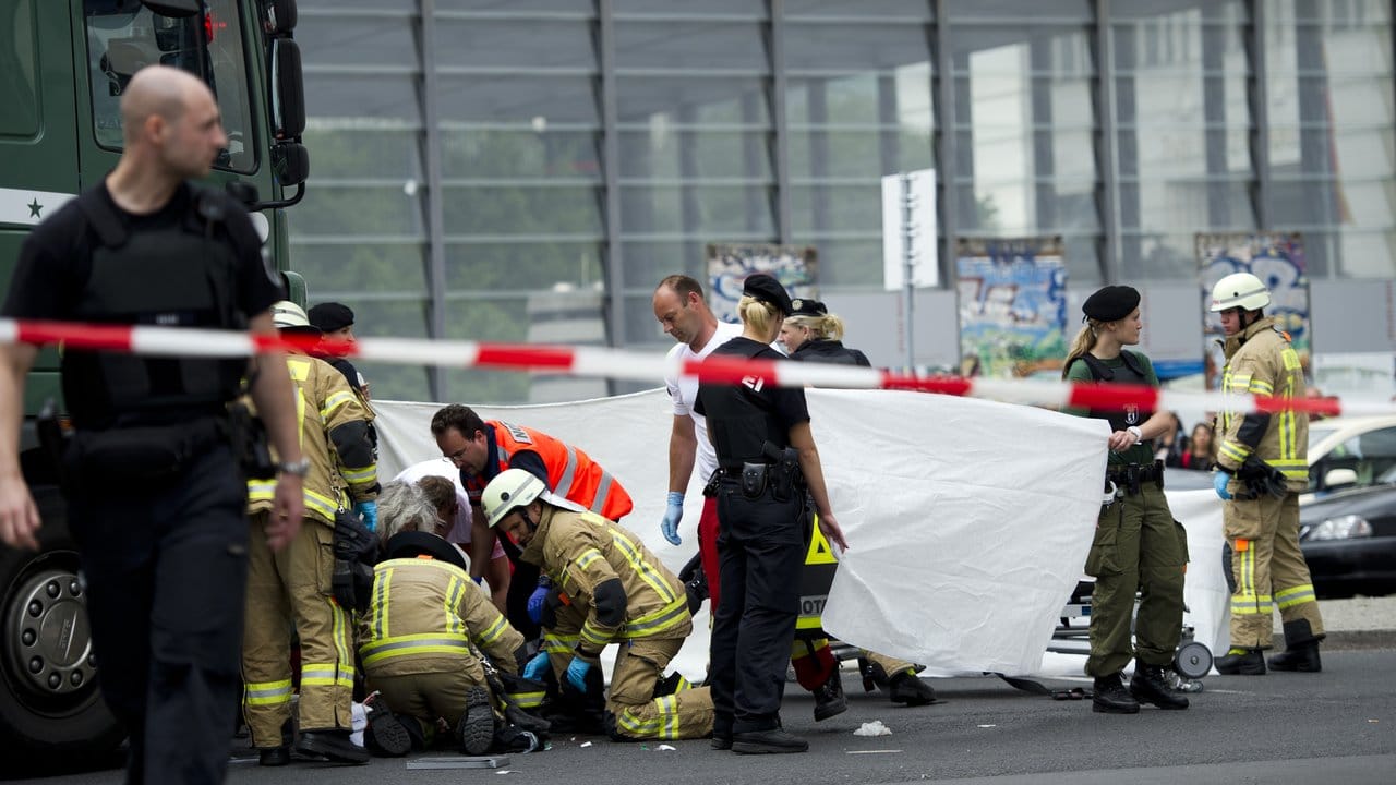 Rettungskräfte helfen auf der Straßenkreuzung am Potsdamer Platz in Berlin einem verletzten Radfahrer, der unter einem Lastwagen liegt.