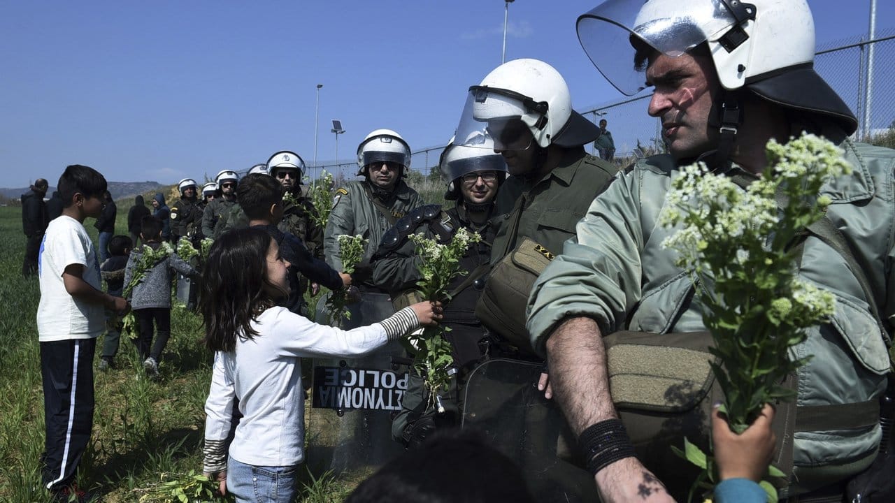 Kinder von Migranten bieten Bereitschaftspolizisten Blumen am Zaun eines Flüchtlingslagers an.