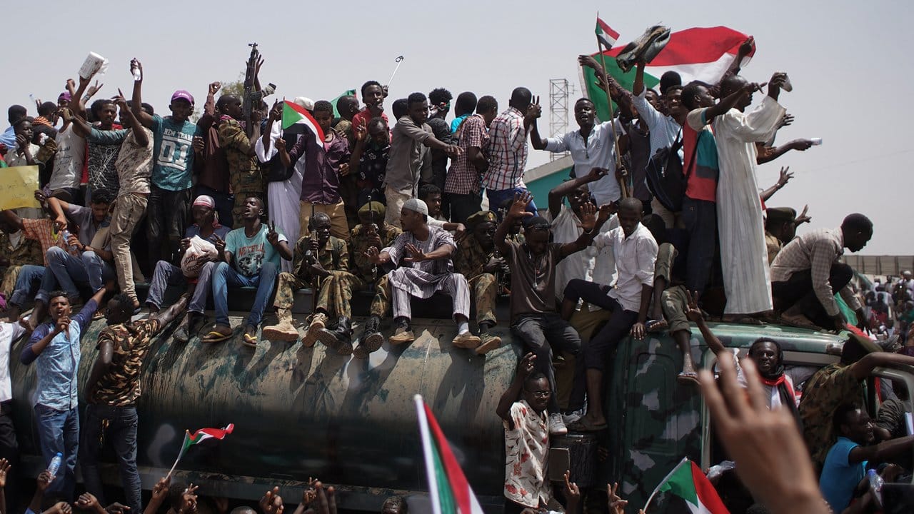 Demonstranten und Soldaten sitzen und stehen auf einem Militärfahrzeug vor dem Verteidigungsministerium in Khartum.