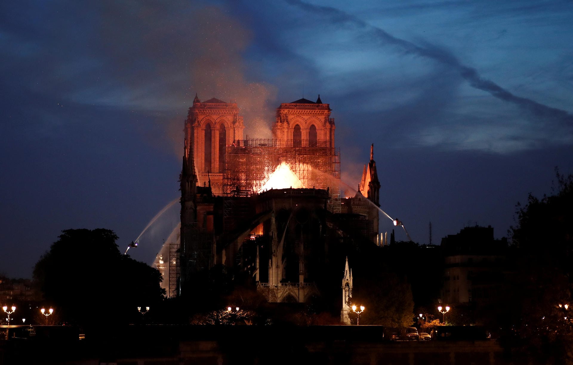 Gespenstisch ist Notre-Dame von den Flammen erleuchtet. Feuerwehrleute pumpen von Kränen Wasser in das Feuer.