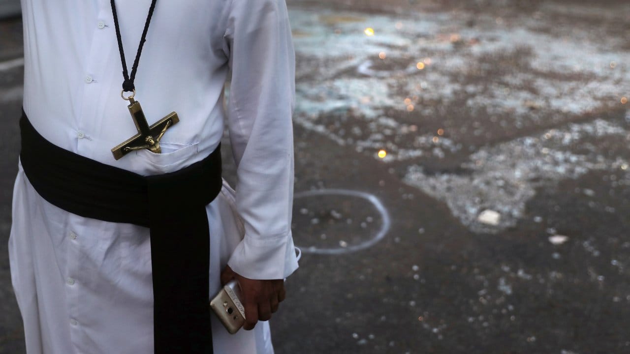 Gefahrenzone: Ein katholischer Priester steht neben Glasscherben vor der Kirche St.