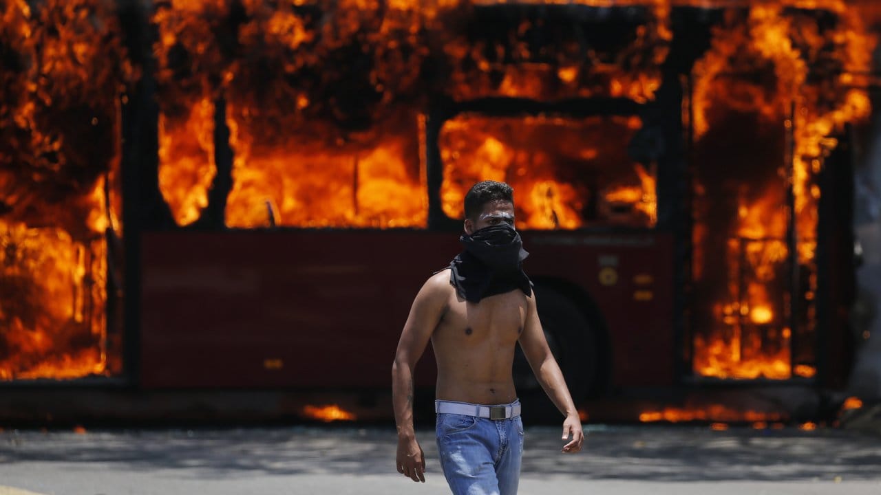 Ein Demonstrant steht vor einem brennenden Bus.