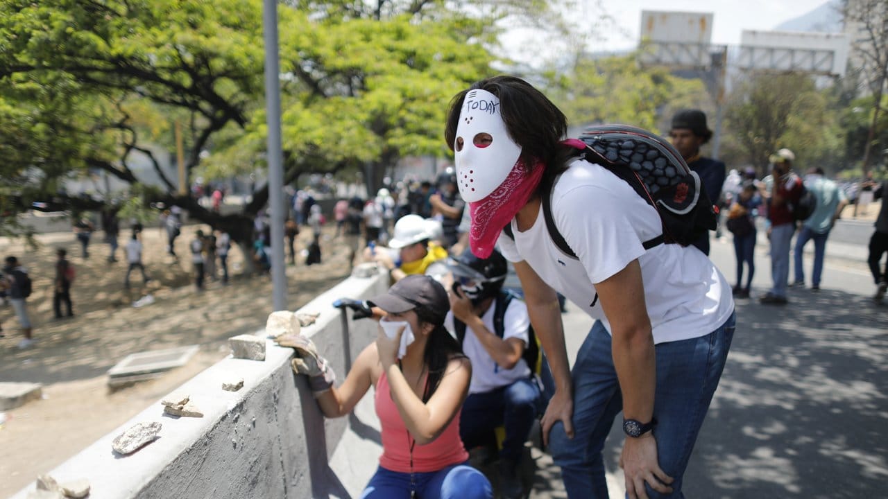 Demonstranten gegen Maduros Regierung verdecken ihre Gesichter, nachdem Sicherheitskräfte Tränengas eingetzt haben.