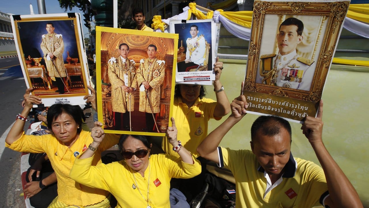 Menschen tragen bei den Feierlichkeiten Bilder des neuen Königs von Thailand.