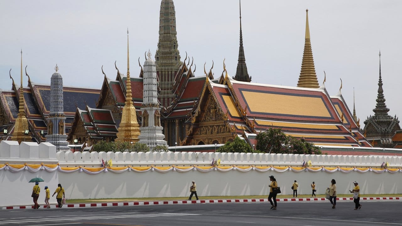 In Gelb gekleidete Menschen halten sich während der Krönung des neuen Königs von Thailand am Großen Palast auf.