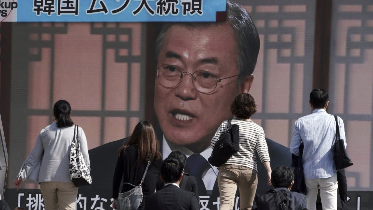 Passanten gehen an einem Bildschirm vorbei, auf dem eine Nachrichtensendung mit dem südkoreanischen Präsidenten Moon Jae-in zu sehen ist.