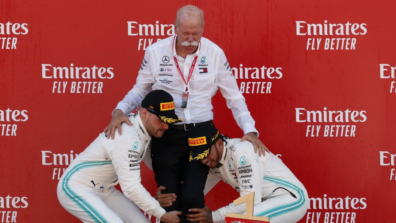 Lewis Hamilton (r) und Valtteri Bottas (l) heben Daimler-Vorstand Dieter Zetsche auf dem Podium in die Luft.