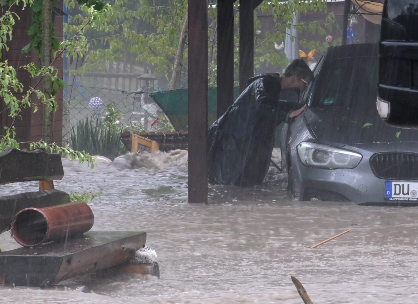 Plaue: Ein Mann steht im vom Wasser überfluteten Garten neben einem Auto.
