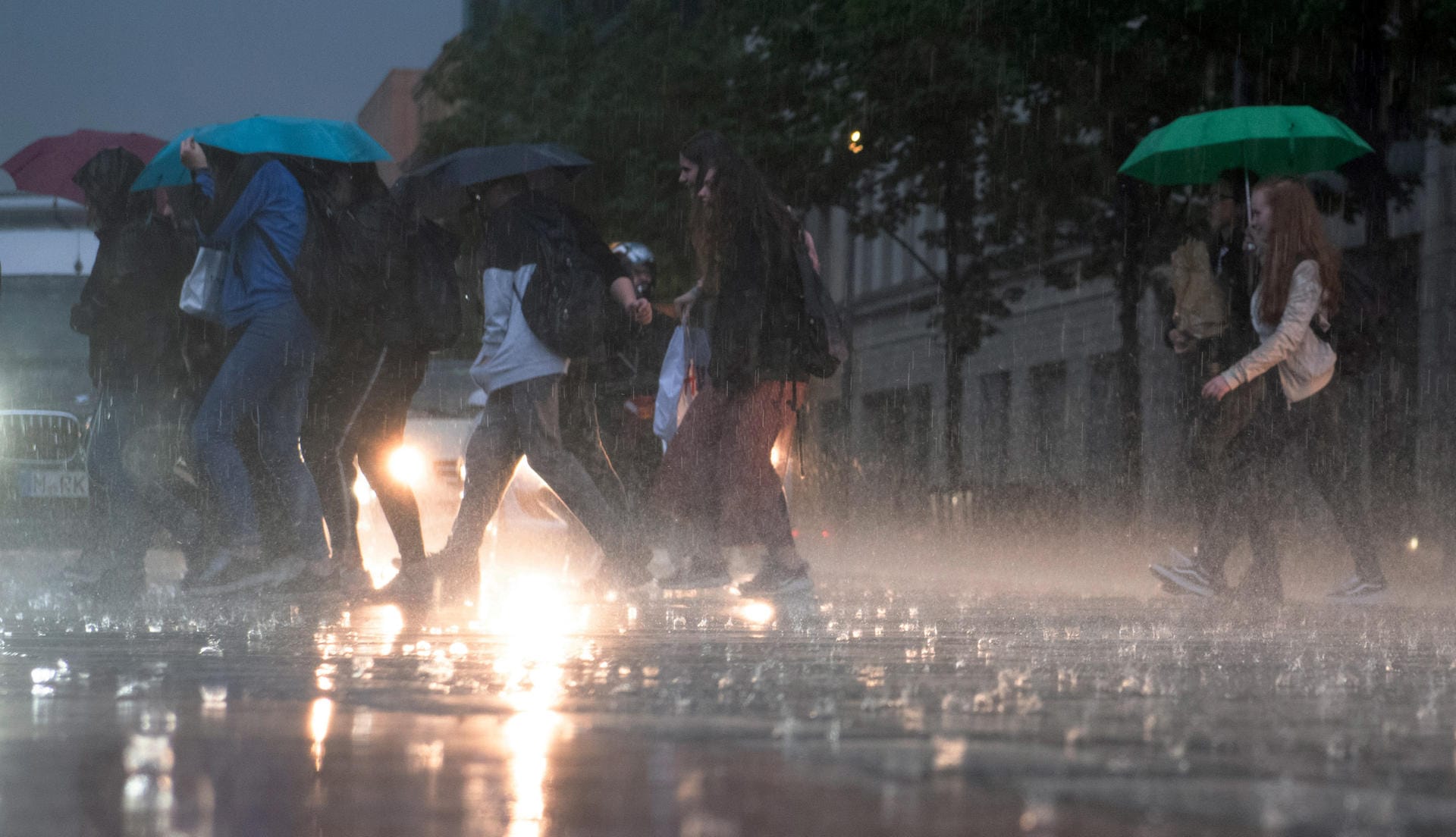 Heftiger Regen in Berlin: Passanten mit Regenschirmen laufen über die Straße. Die Berliner Feuerwehr musste wegen der Gewitter zu zahlreichen Einsätzen ausrücken und rief den Ausnahmezustand aus.