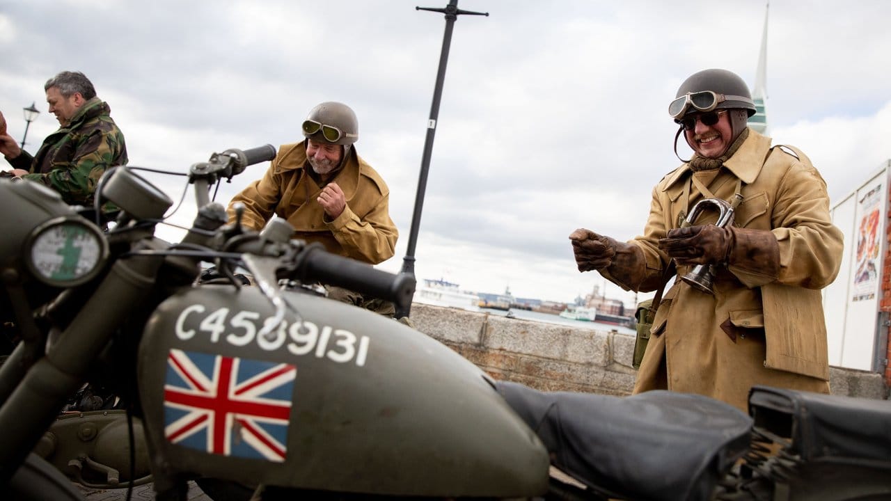 Drei Briten stehen in historischen Uniformen mit historischen Motorrädern in der Altstadt von Portsmouth.