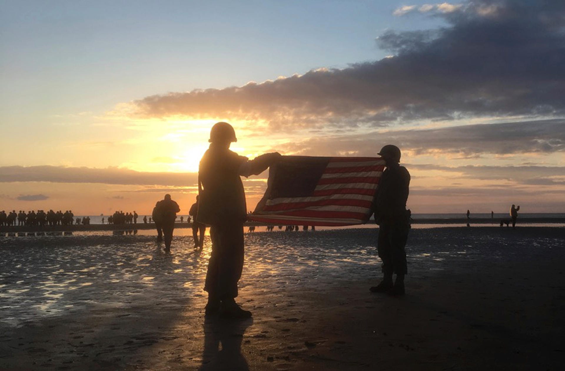 Frankreich, Vierville-Sur-Mer: Zwei Männer in historischen Uniformen halten bei Sonnenaufgang eine amerikanische Flagge als Teil der Veranstaltungen anlässlich des 75. Jahrestags des D-Day am Omaha Beach.