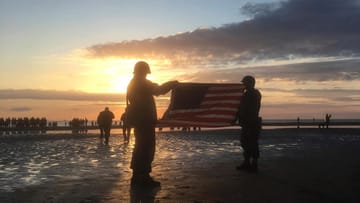 Frankreich, Vierville-Sur-Mer: Zwei Männer in historischen Uniformen halten bei Sonnenaufgang eine amerikanische Flagge als Teil der Veranstaltungen anlässlich des 75. Jahrestags des D-Day am Omaha Beach.