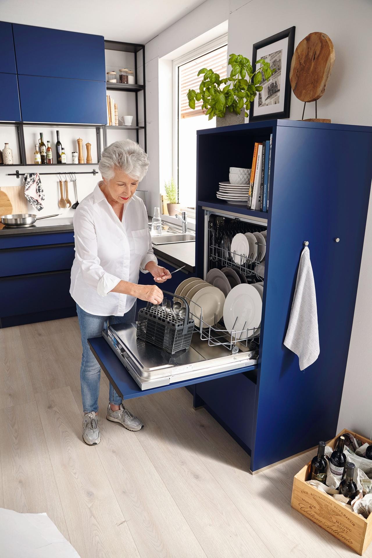 Seniorin steht vor Geschirrspüler auf Hüfthöhe: Viele Küchengeräte lassen sich auch erhöht einbauen, der Geschirrspüler etwa.