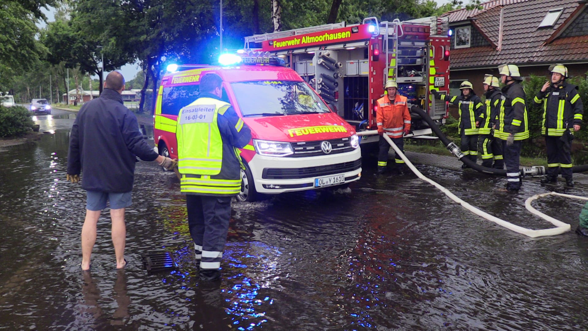 Niedersachsen, Kirchhatten: Nach einem Unwetter mit Starkregen stehen Feuerwehrleute auf einer überfluteten Straße und legen Schläuche, um Wasser abzupumpen.