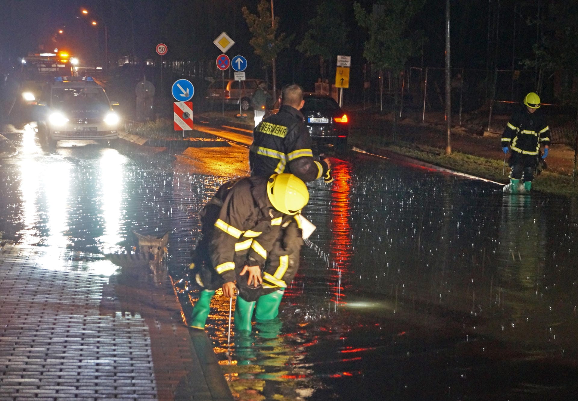 Brandenburg, Dallgow-Döberitz: Feuerwehrleute arbeiten nach dem Sommergewitter mit heftigen Regenfällen an einer überfluteten Straße.