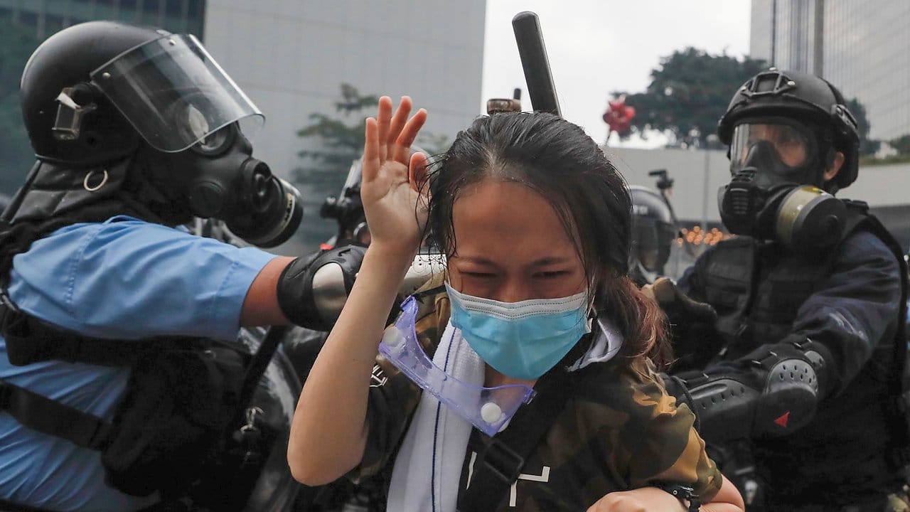 Polizisten drücken eine Demonstrantin gegen eine Absperrung.