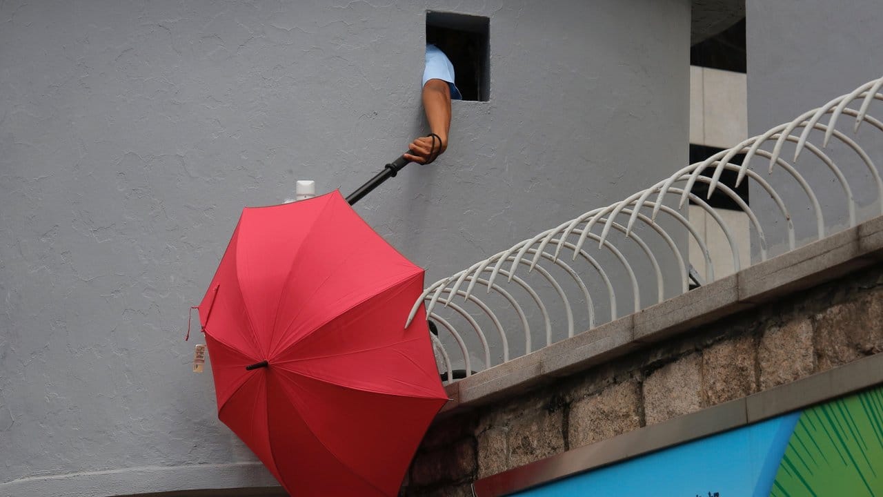 Ein Polizist versucht, einen Regenschirm zu entfernen, der den Blick der Überwachungskameras vor dem Polizeipräsidium in Hongkong blockiert.
