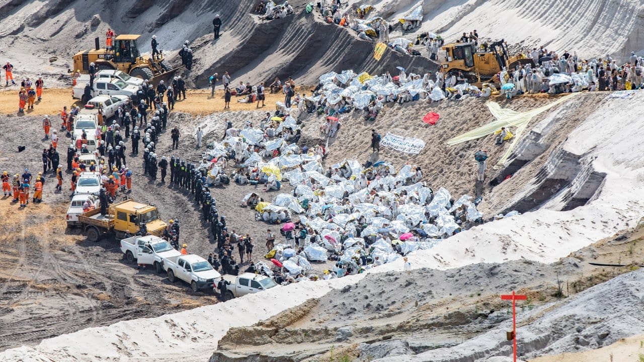 Umweltaktivisten schützen sich mit Rettungsdecken vor der Sonne, nachdem sie im Tagebau Garzweiler von Polizisten eingekesselt wurden.