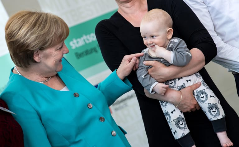 Die Bundeskanzlerin Angela Merkel streichelt ein Baby bei einer Preisverleihung. Ihr Nachname wurde inzwischen offiziell auch als Vorname anerkannt.