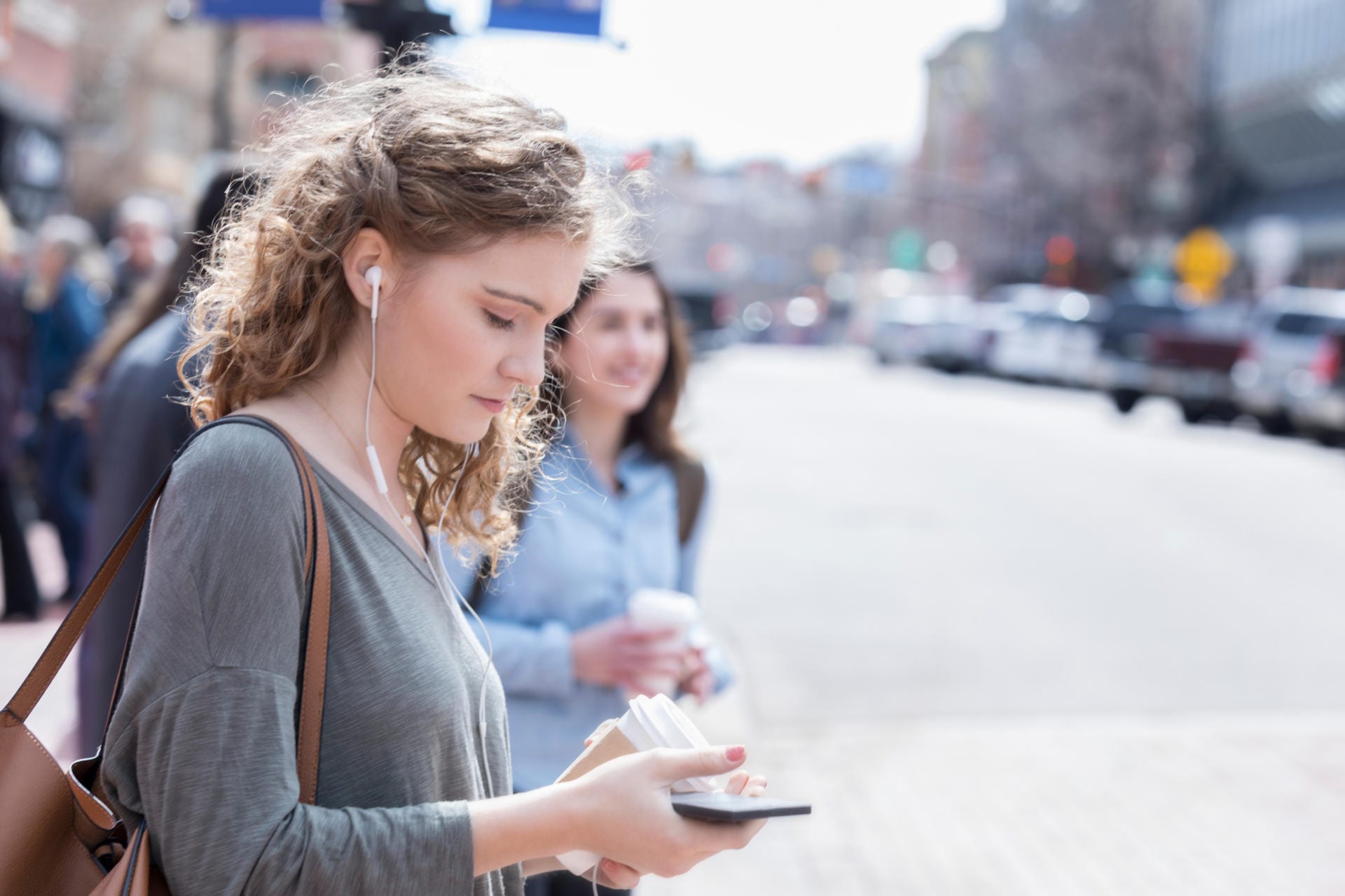 Junge Frau schaut an einer Kreuzung aufs Smartphone: In der kalifornischen Kleinstadt Montclair werden Fußgänger, die ihr Mobilgerät benutzen, während sie die Straße überqueren, mit bis zu 500 Dollar bestraft.