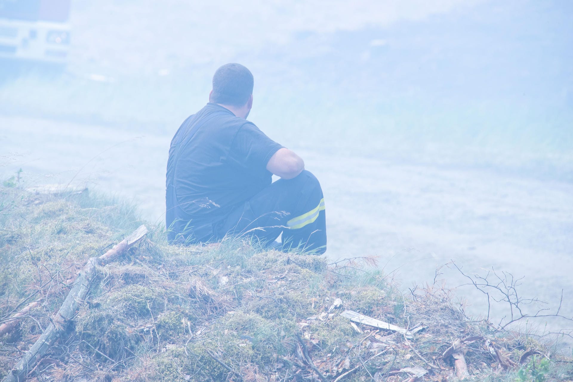 Ein erschöpfter Feuerwehrmann sitzt in einer Rauchwolke im brennenden Wald in der Nähe der kleinen Ortschaft Alt Jabel.