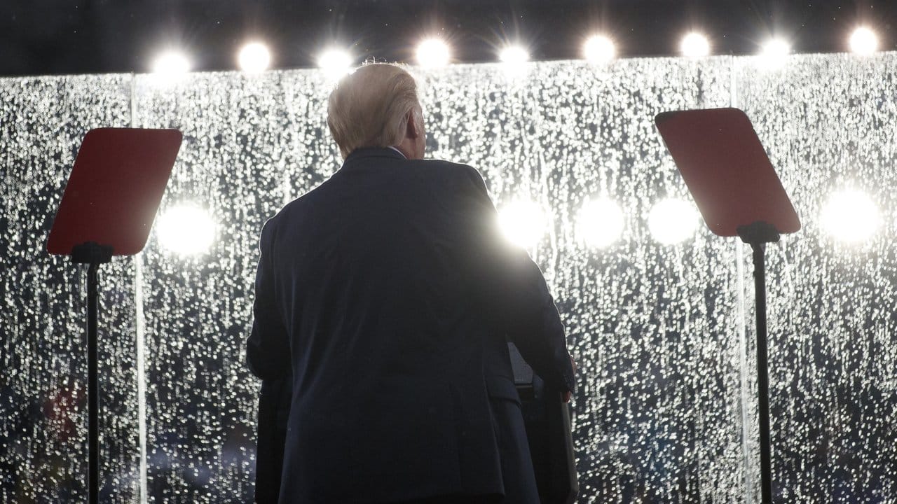 Donald Trump hält bei Regen seine Rede hinter einem Sicherheitsglas.