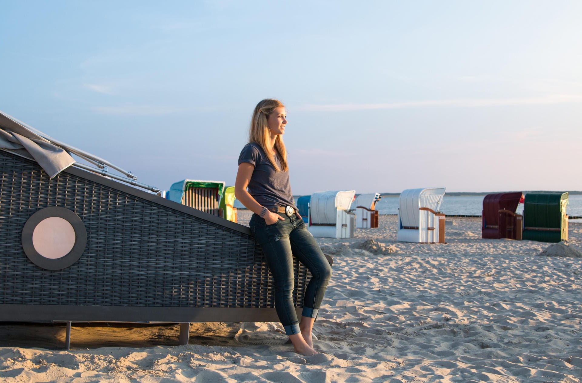 Frau steht an Strandschlafkorb: Auf der Nordseeinsel Föhr können Sie an fünf Standorten in speziellen Strandkörben übernachten.