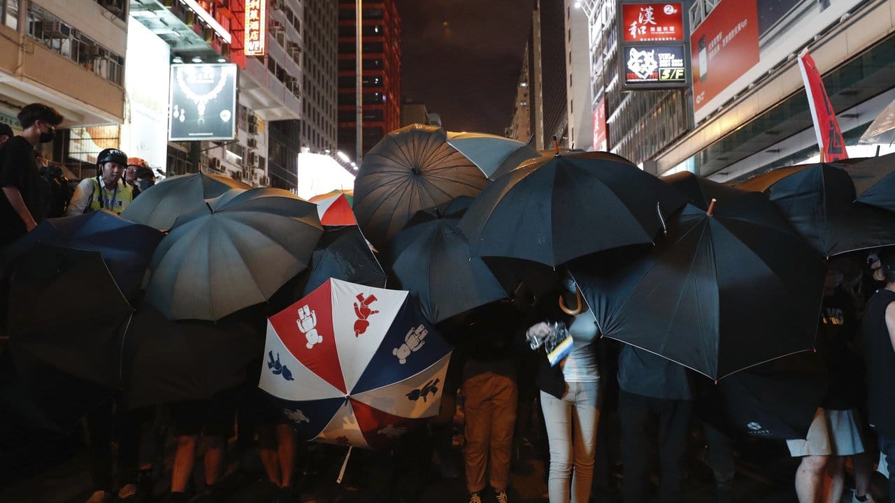 Demonstranten verbergen ihre Gesichter hinter Regenschirmen.