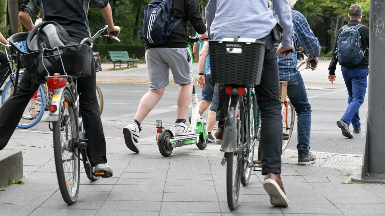 Ein E-Tretroller zwischen Fahrrädern und Autos im Straßenverkehr.