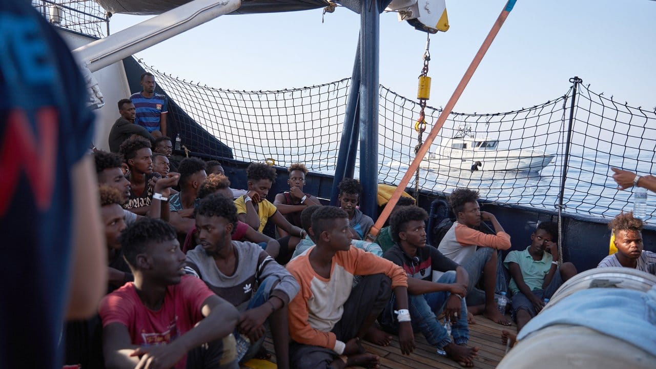 Wohin? Flüchtlinge an Bord des Seenotrettungsschiffs "Alan Kurdi", während ein Boot der italienischen Guardia di Finanza vorbei fährt.