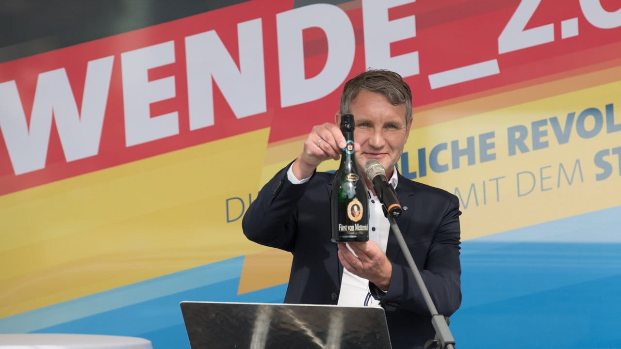 Symbolisches Geschenk für vermeintliche Verfassungsschützer im Publikum: Björn Höcke mit einer Flasche Sekt.