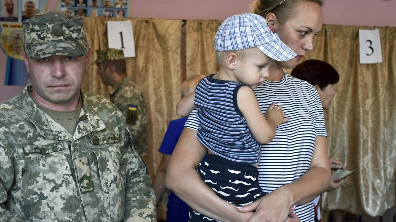 Ein Soldat und eine Frau mit einem Kind kommen in ein Wahllokal in Kramatorsk.