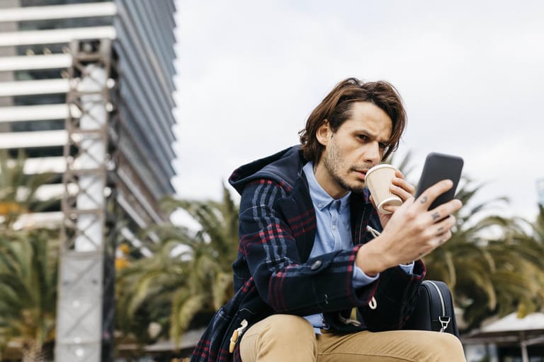 Ein Mann trinkt Kaffee und blickt auf sein Smartphone