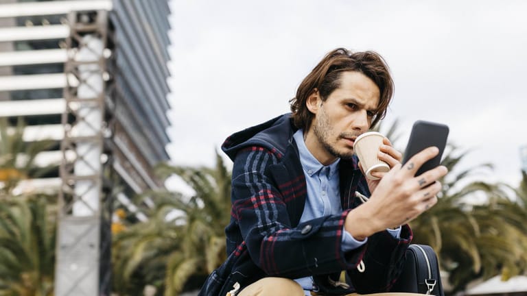 Ein Mann trinkt Kaffee und blickt auf sein Smartphone