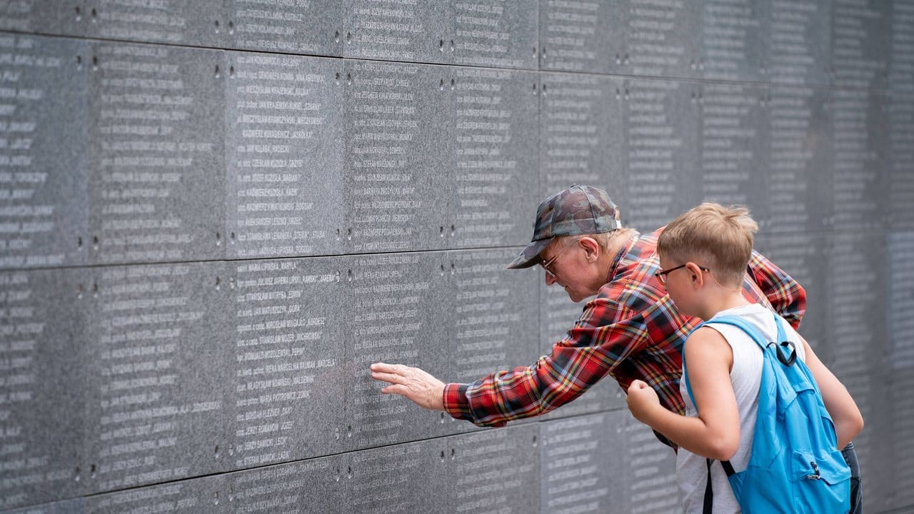 Besucher lesen auf einer Gedenkmauer Namen von Opfern des Warschauer Aufstands.
