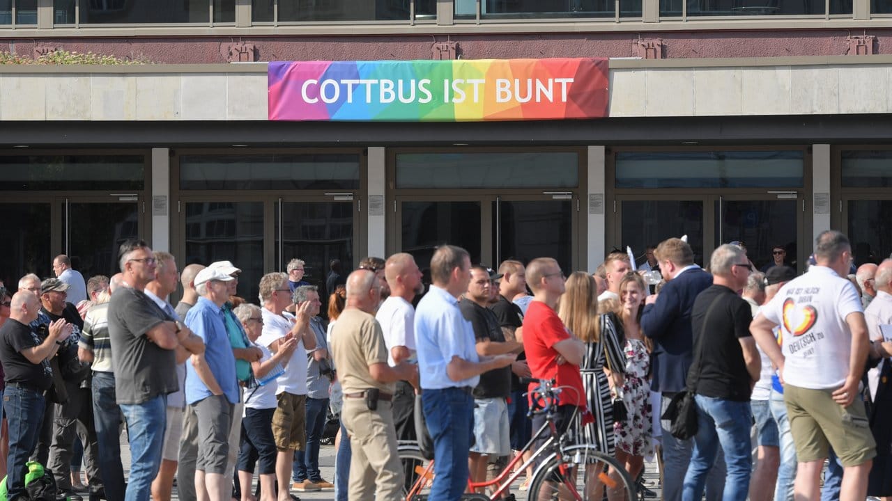 Teilnehmer des Wahlkampfauftakts der AfD-Jugendorganisation Junge Alternative stehen vor einem Transparent an der Stadthalle mit der Aufschrift "Cottbus ist bunt".