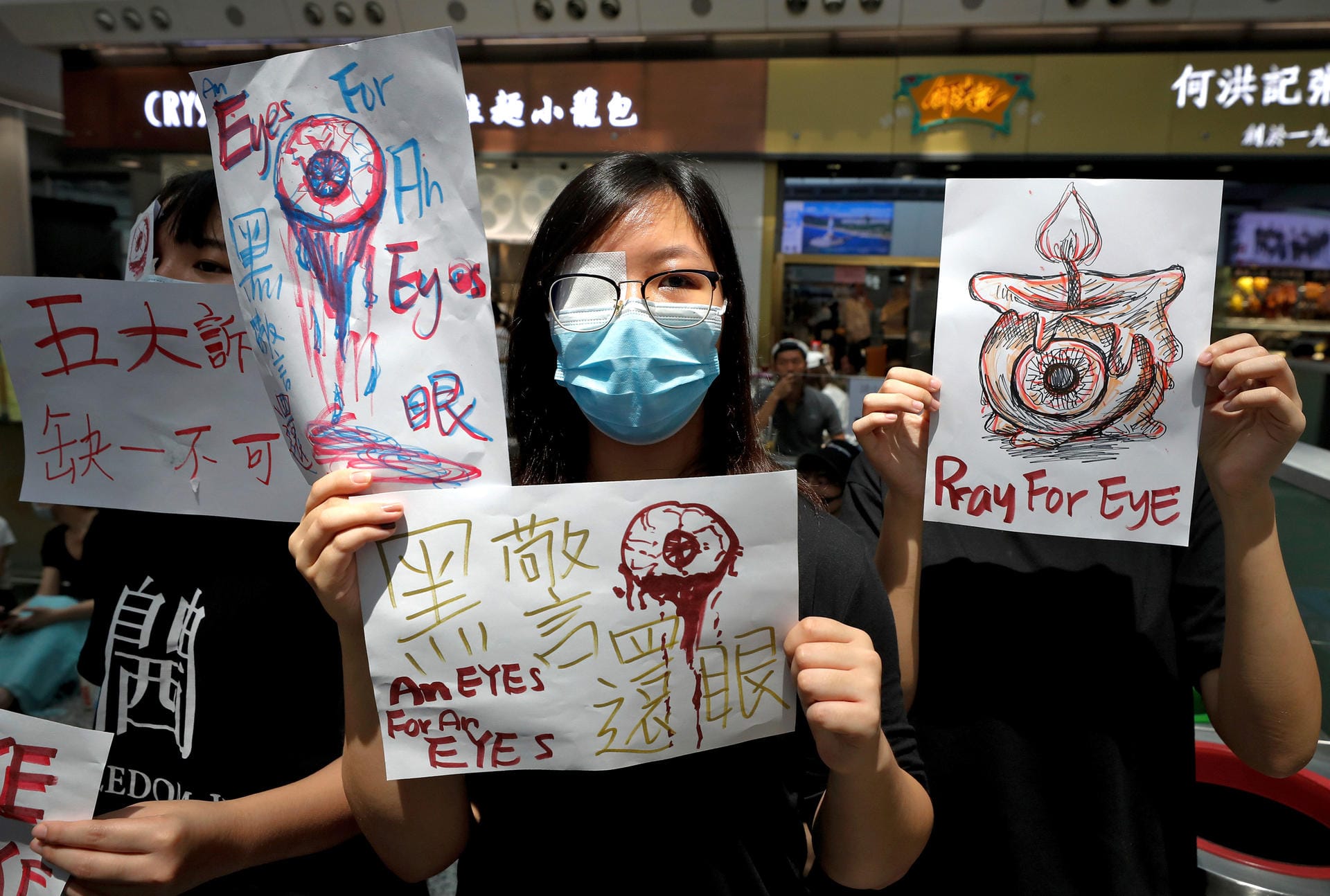 Demonstranten halten in der Ankunftshalle des Flughafens Schilder mit der Aufschrift "Pray for eye": Nach Angaben der Protestierenden hatte die Polizei bei den gewaltsamen Auseinandersetzungen einer Frau ins Auge geschossen.