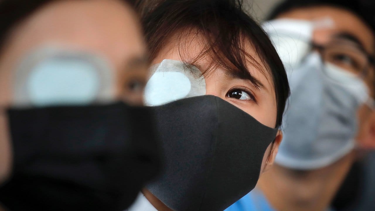 Augenklappe und Mundschutz sollen den Protest gegen die Polizei symbolisieren, die bei den Auseinandersetzungen im Flughafen eine Frau mit einem Gummigeschoss im Gesicht schwer verletzt haben soll.