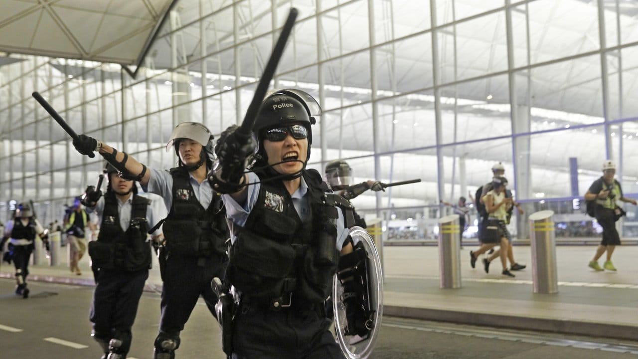 Polizisten mit Schlagstöcken im Hongkonger Flughafen an.