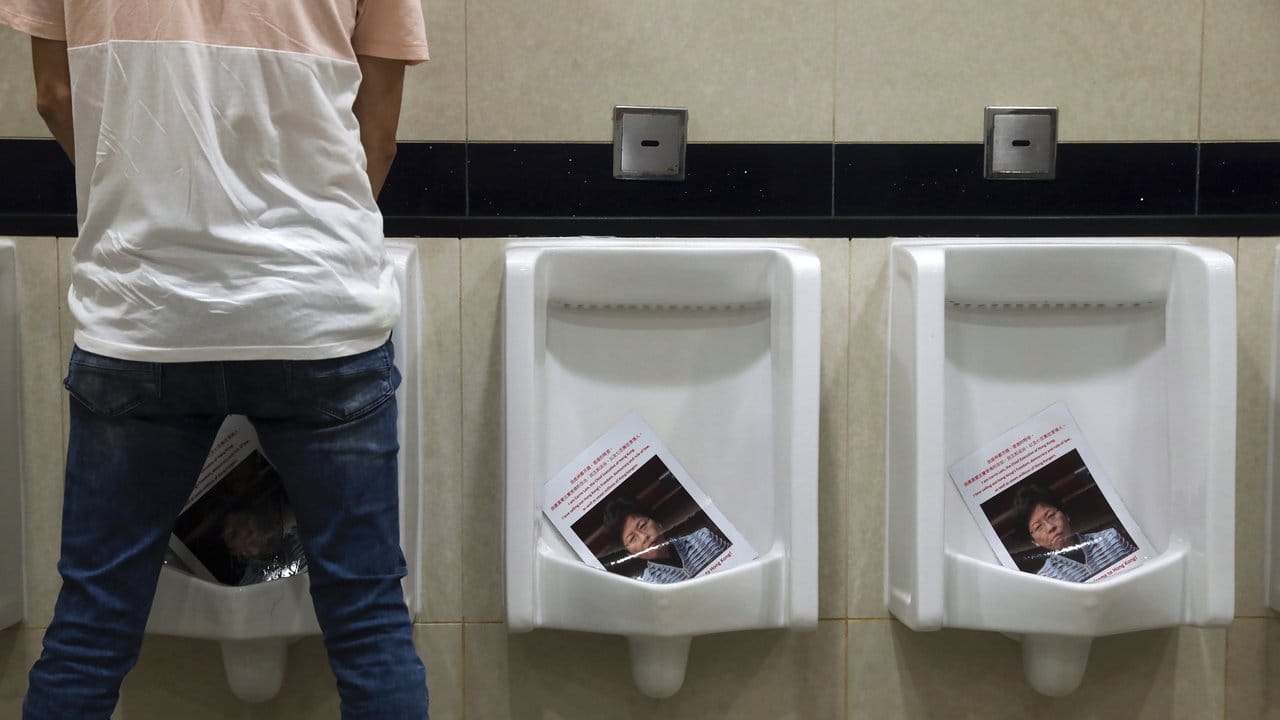 Ein Mann uriniert während einer Demonstration am Flughafen in einer Toilette auf Fotos von Carrie Lam, Regierungschefin von Hongkong.