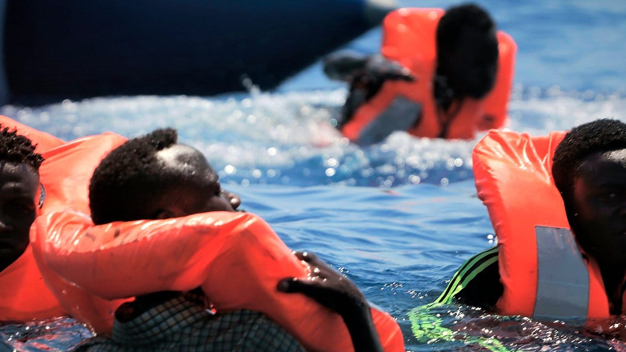 Flüchtlinge schwimmen mit Rettungswesten im Meer, bevor sie vom Rettungsschiff "Ocean Viking" aufgenommen werden.